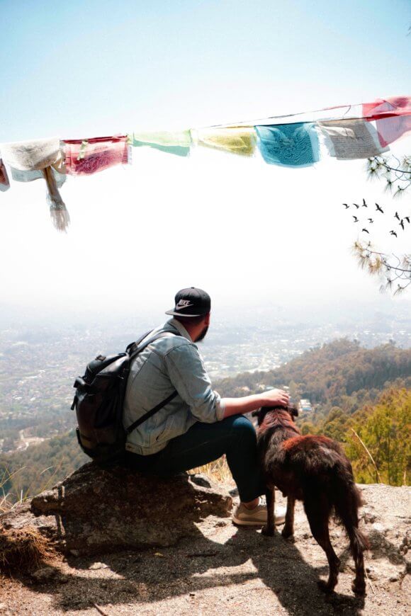 man-sitting-on-rock-petting-dog-outdoors-2204542-580x870
